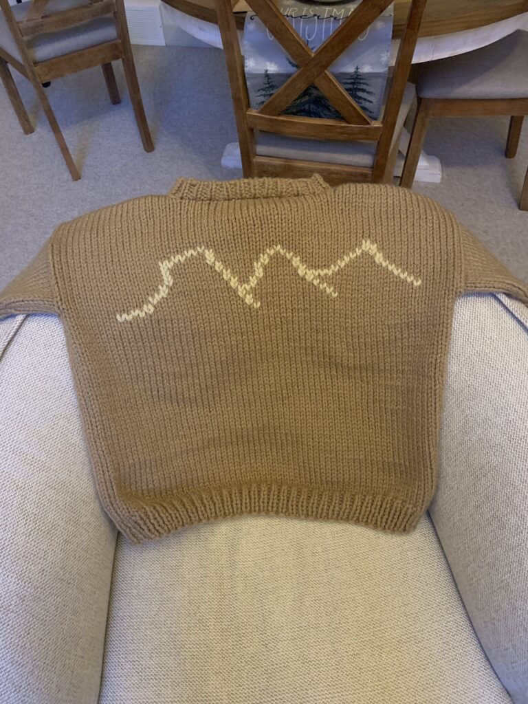 beige sweater with three sisters mountain range on it